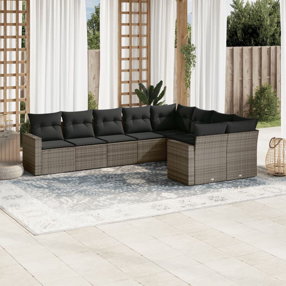 Rattan-Ecksofa mit schwarzen Kissen auf einer Terrasse mit Teppich und Korb angeordnet.