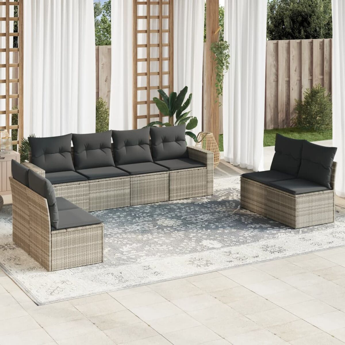 Outdoor-Sitzgruppe mit grauen Kissen, beigem Korbsessel, zwei Stühlen und einem gemusterten Teppich.