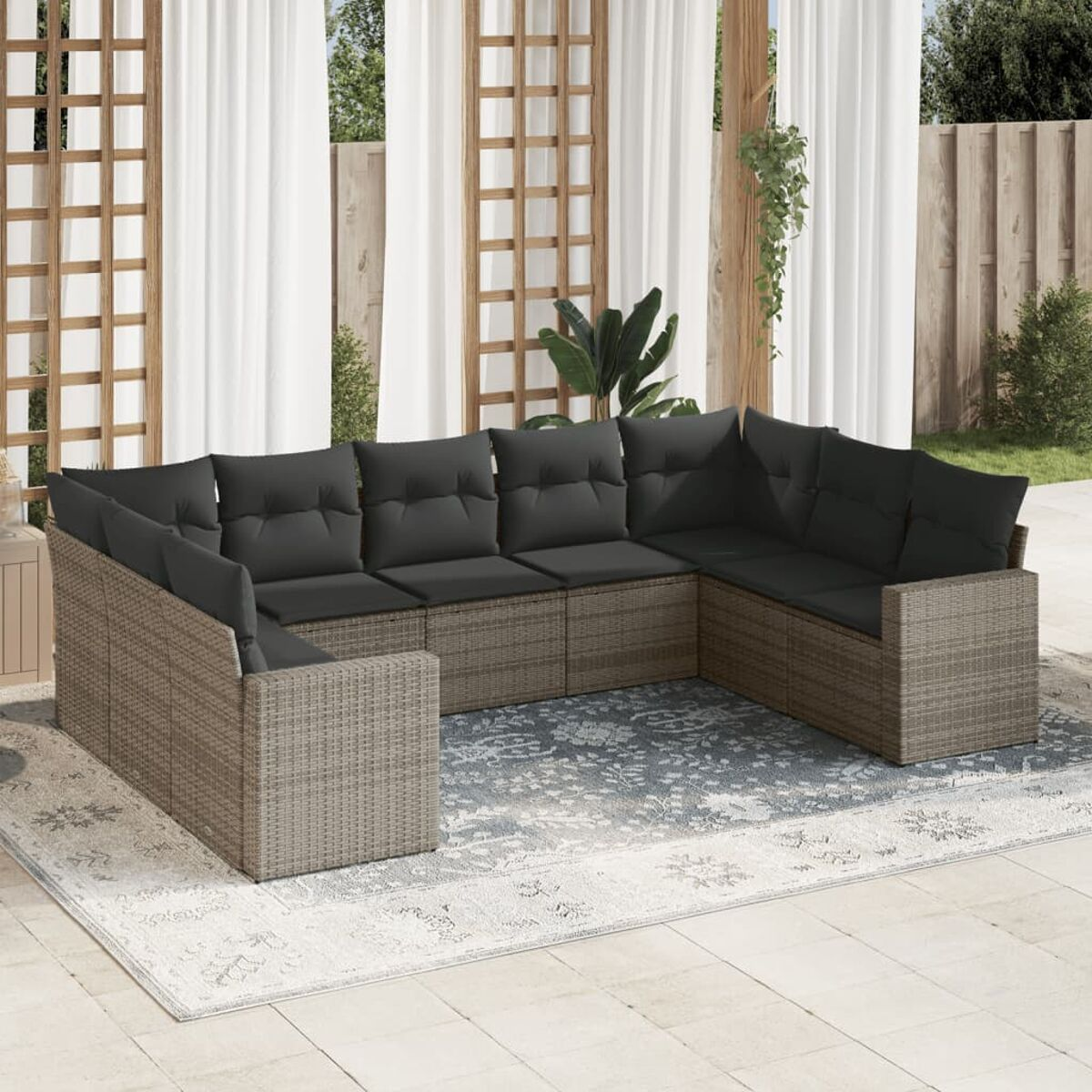 Geflochtenes Ecksofa-Set mit grauen Kissen auf einem Teppich. Außenbereich mit Vorhängen und Pflanzen.