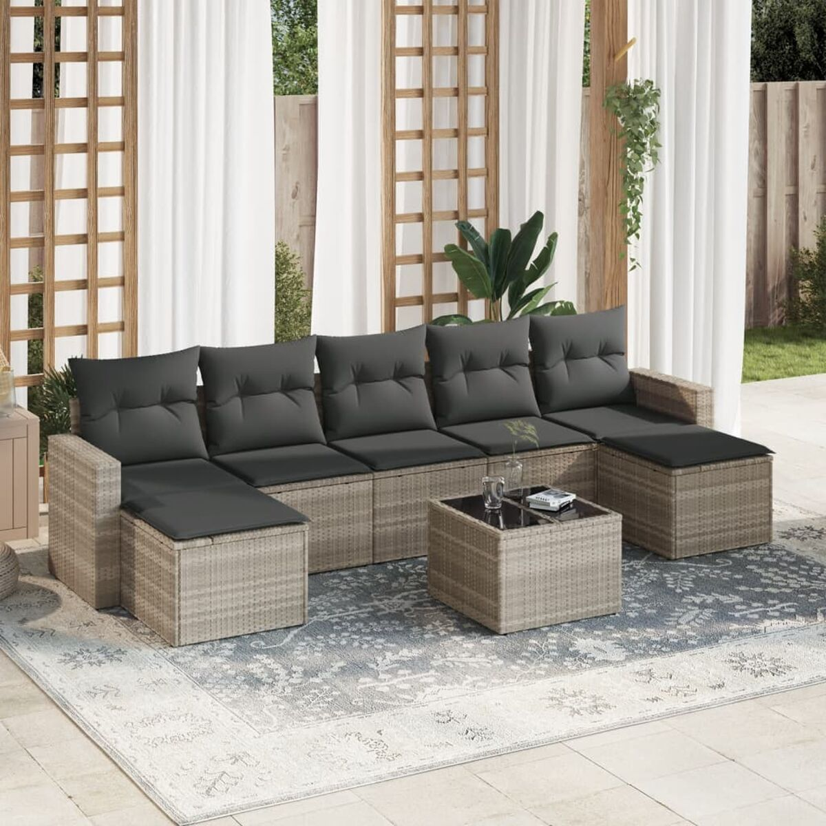 Divano componibile in rattan con cuscini grigi e tavolo quadrato. Include tende, tappeto e pergola.