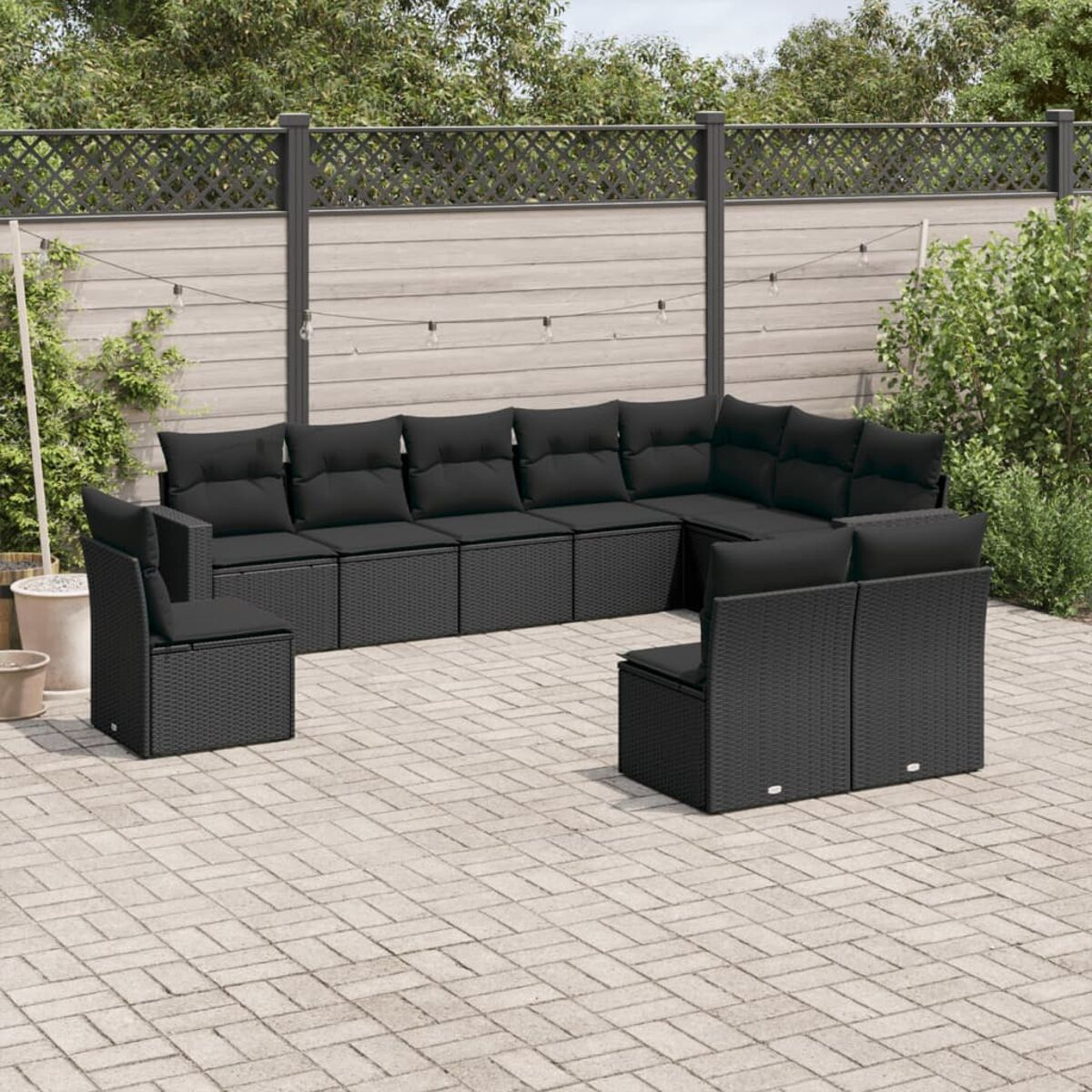 Schwarzes Outdoor-Ecksofa mit schwarzen Kissen, kleinem Tisch und Getränken auf einer Terrasse, Zaun im Hintergrund.