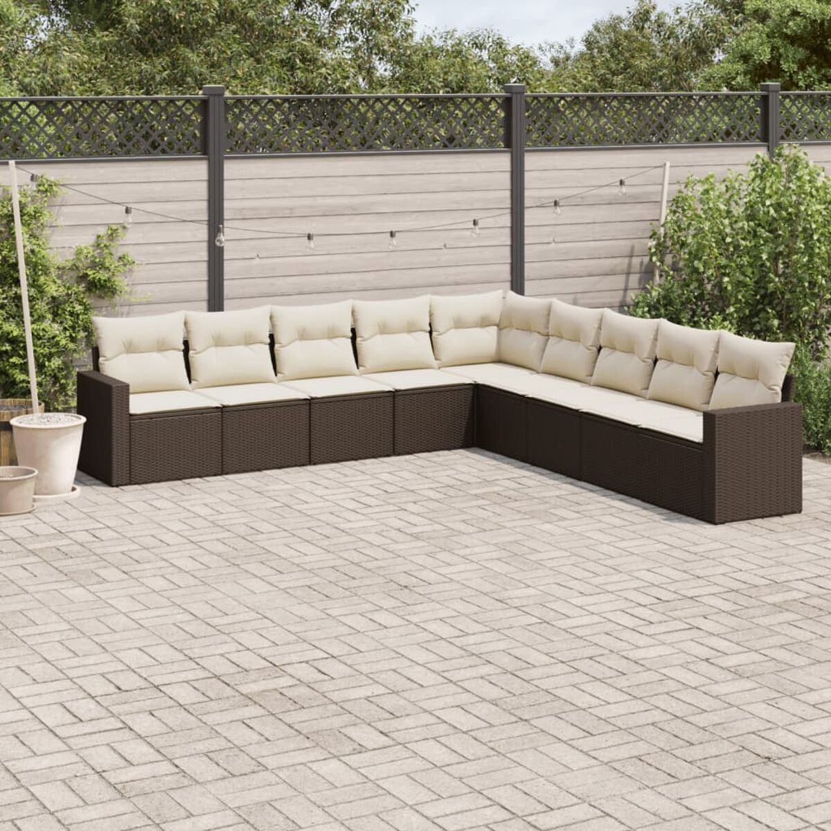 Braunes Rattansofa mit cremefarbenen Kissen. Szene mit Zaun, Backstein-Terrasse und Grün.
