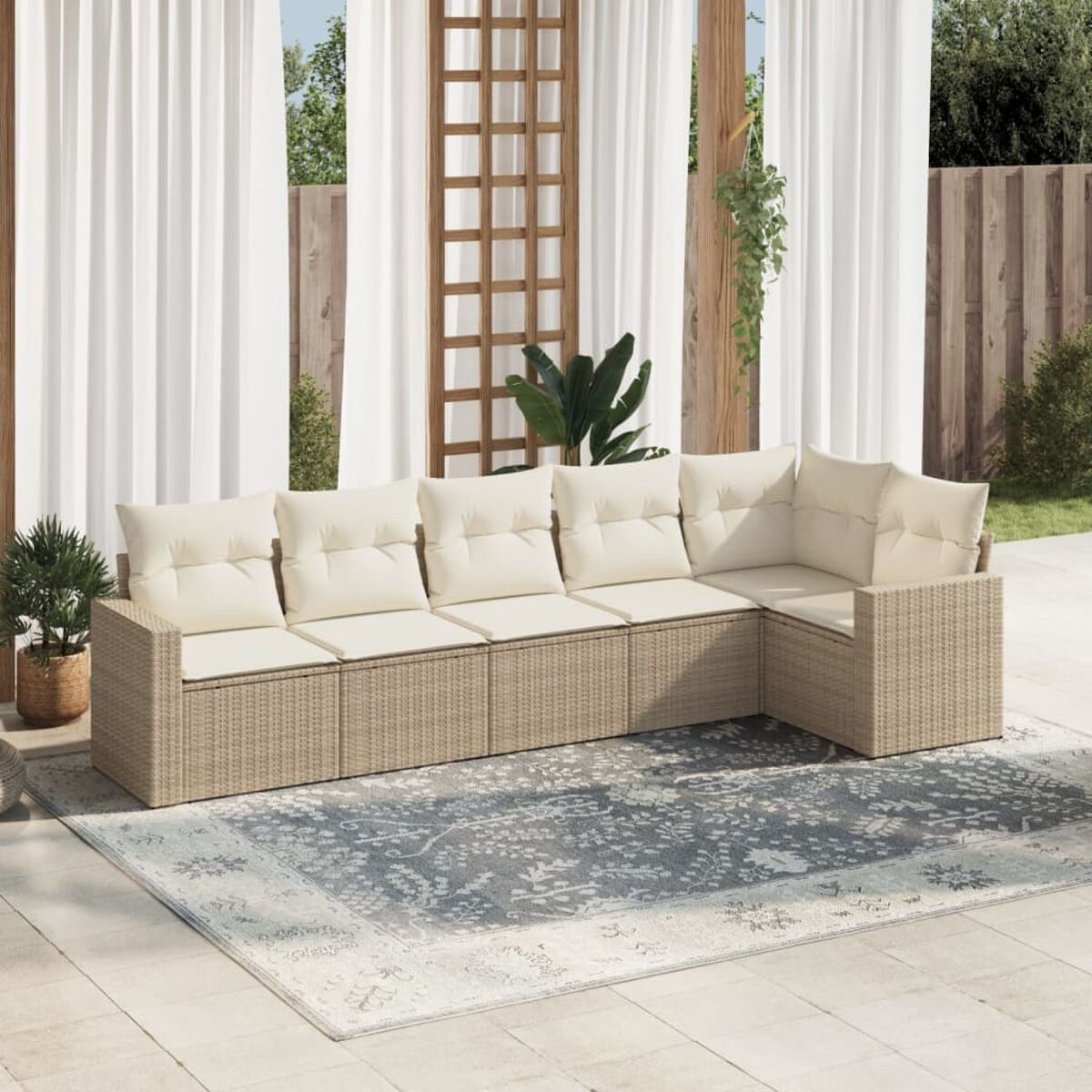 Rattansofa mit cremefarbenen Kissen. Szene mit Vorhängen, Teppich und Grün.