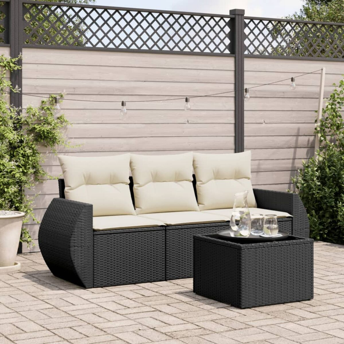 Schwarzes Korbsessel-Sofa mit cremefarbenen Kissen und einem quadratischen Couchtisch, auf einer Ziegelterrasse.