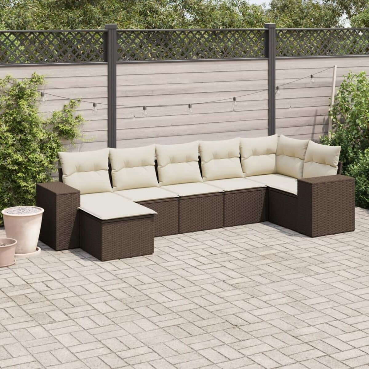 Divano angolare da esterno marrone scuro con cuscini color crema su un patio in mattoni.