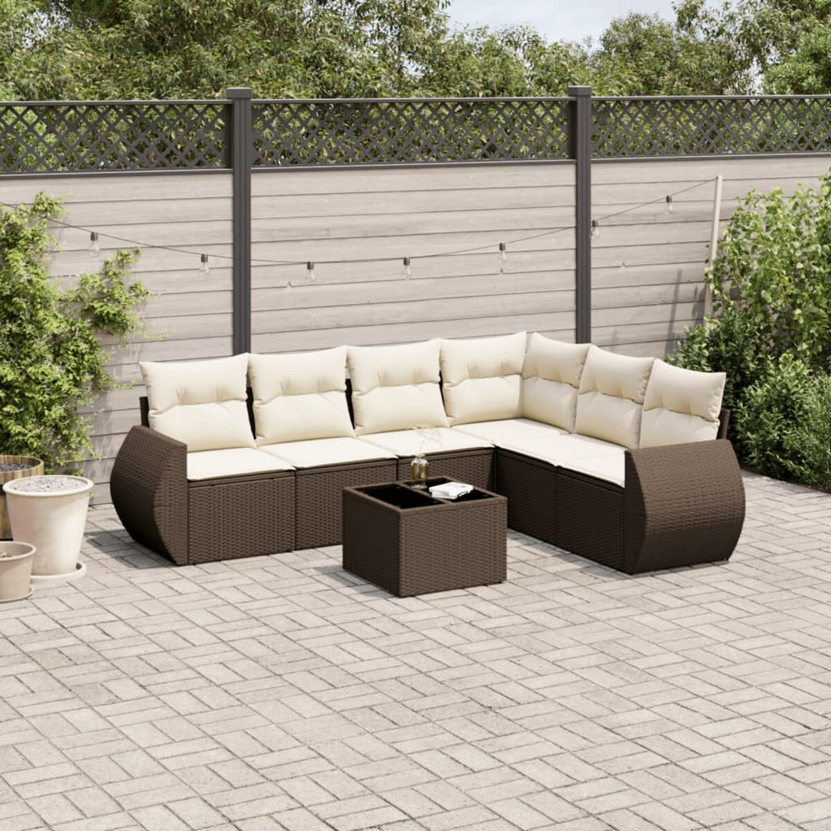 Divano componibile da esterno in vimini marrone con cuscini color crema e tavolino abbinato. Patio in mattoni.