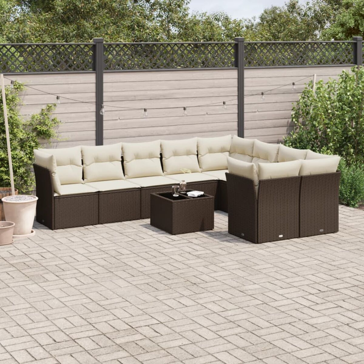 Divano componibile in vimini marrone con cuscini color crema. Patio con tavolo e verde.