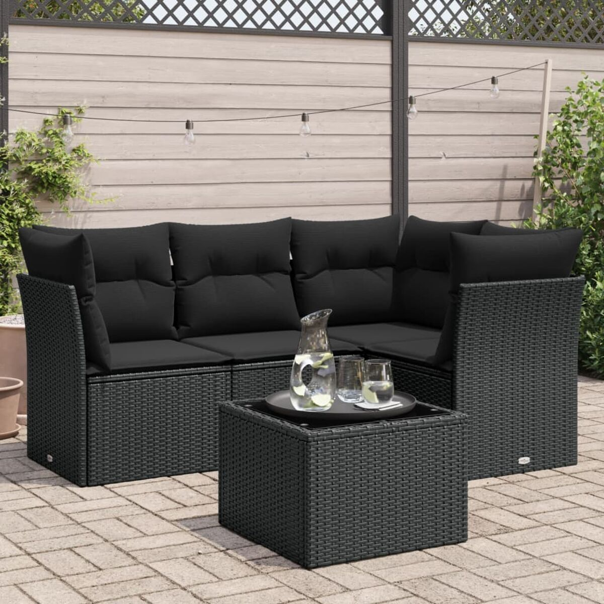 Schwarzes Outdoor-Ecksofa aus Korbgeflecht mit schwarzen Kissen und einem quadratischen Tisch auf einer Ziegelterrasse.