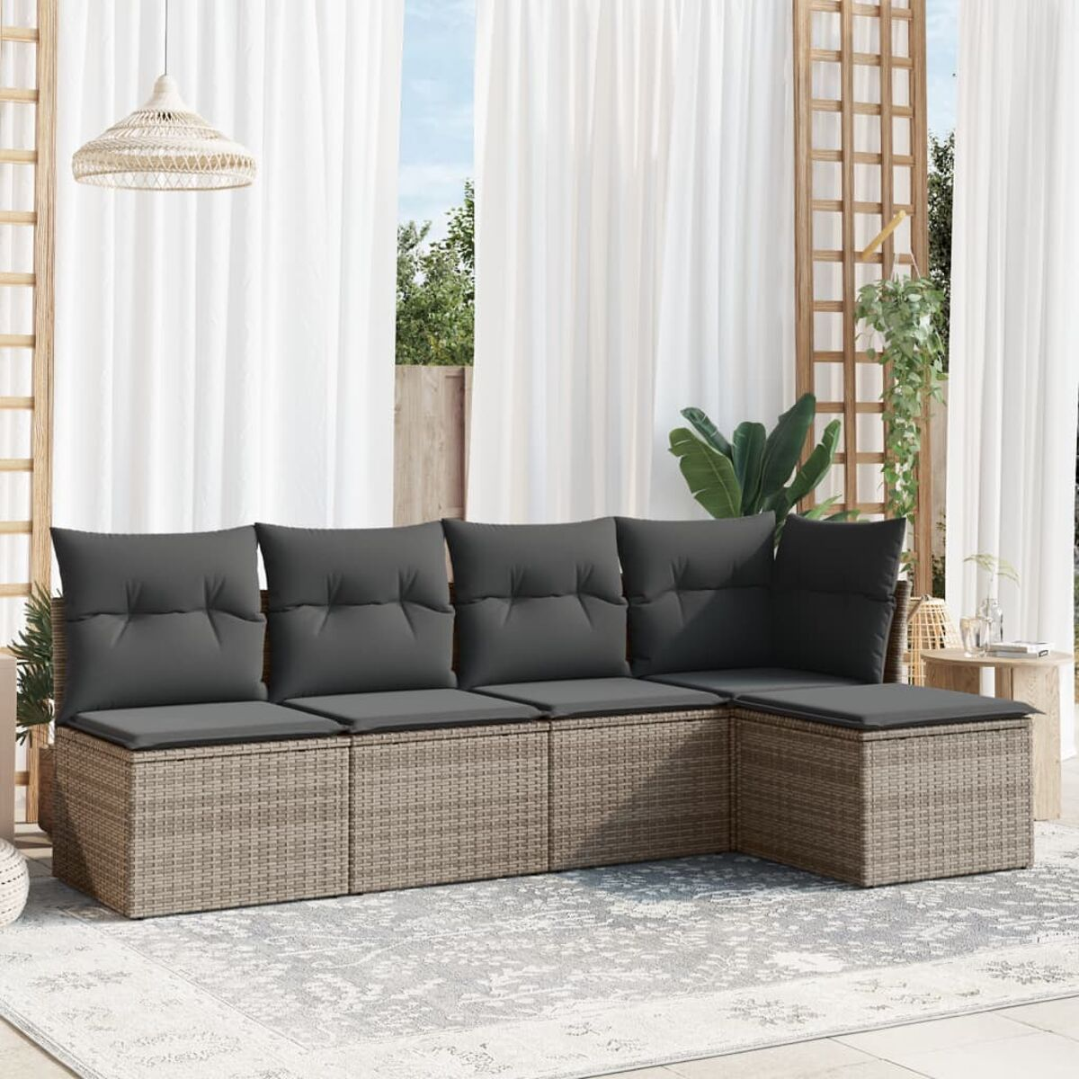 Geflochtenes Outdoor-Sofa-Set mit grauen Kissen. Ein Teppich und weiße Vorhänge im Hintergrund.
