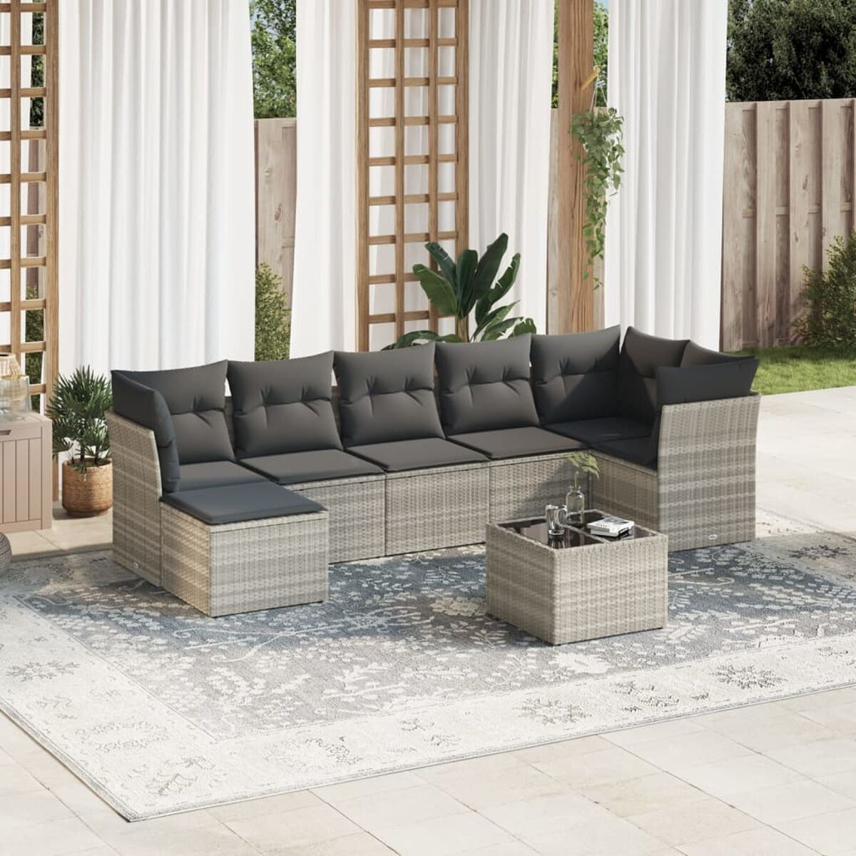 Rattan L-förmige Sofagarnitur, Couchtisch, auf einem gemusterten Teppich. Graue Kissen, Outdoor-Setting.