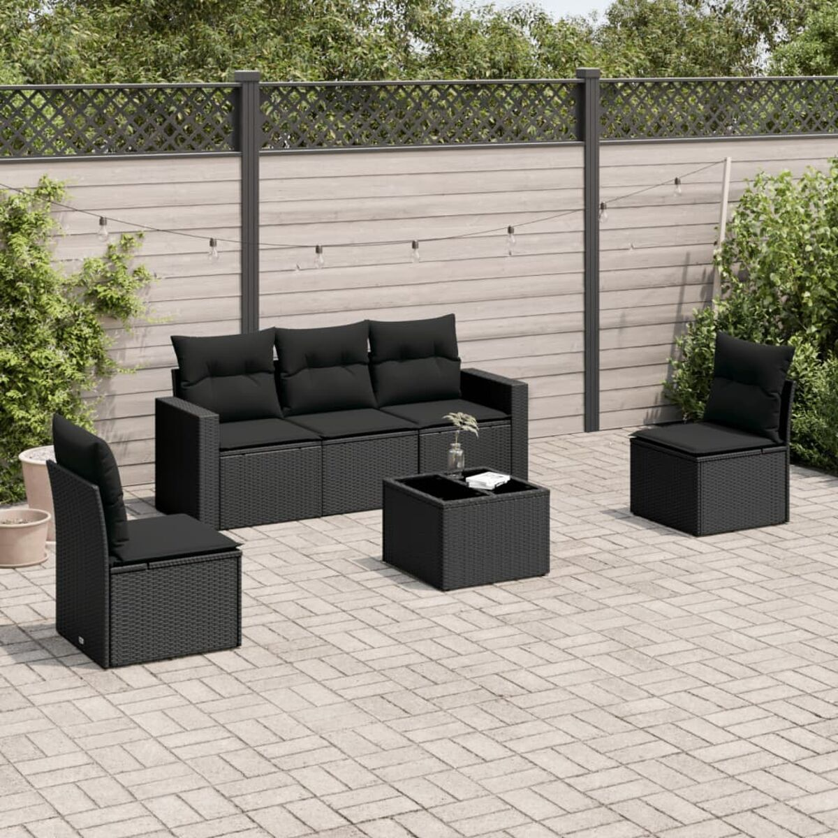 Schwarzes Outdoor-Wicker-Sofa- und Stuhlgarnitur, schwarze Kissen, quadratischer Tisch. Hintergrund mit Ziegelpflaster.