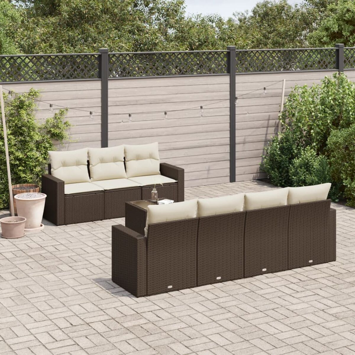 Braunes Outdoor-Sofaset aus Korbgeflecht mit Kissen. Pflanzen und ein Zaun im Hintergrund.