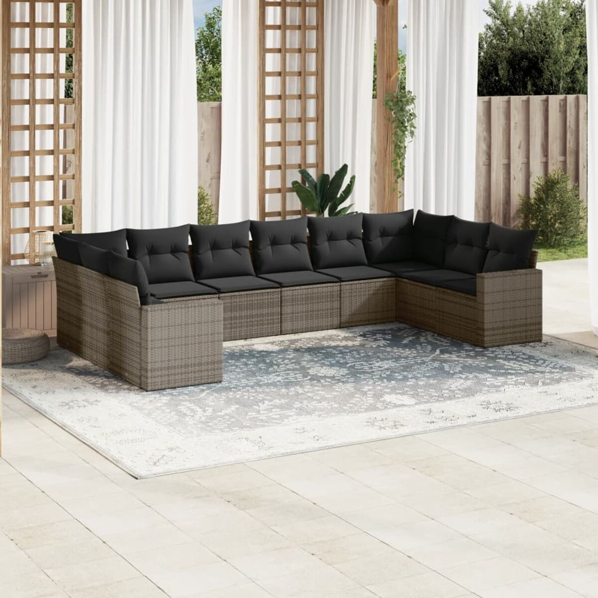 Outdoor-Rattansofa-Set mit Kissen auf einem Teppich. Weiße Vorhänge und Holzzaun im Hintergrund.