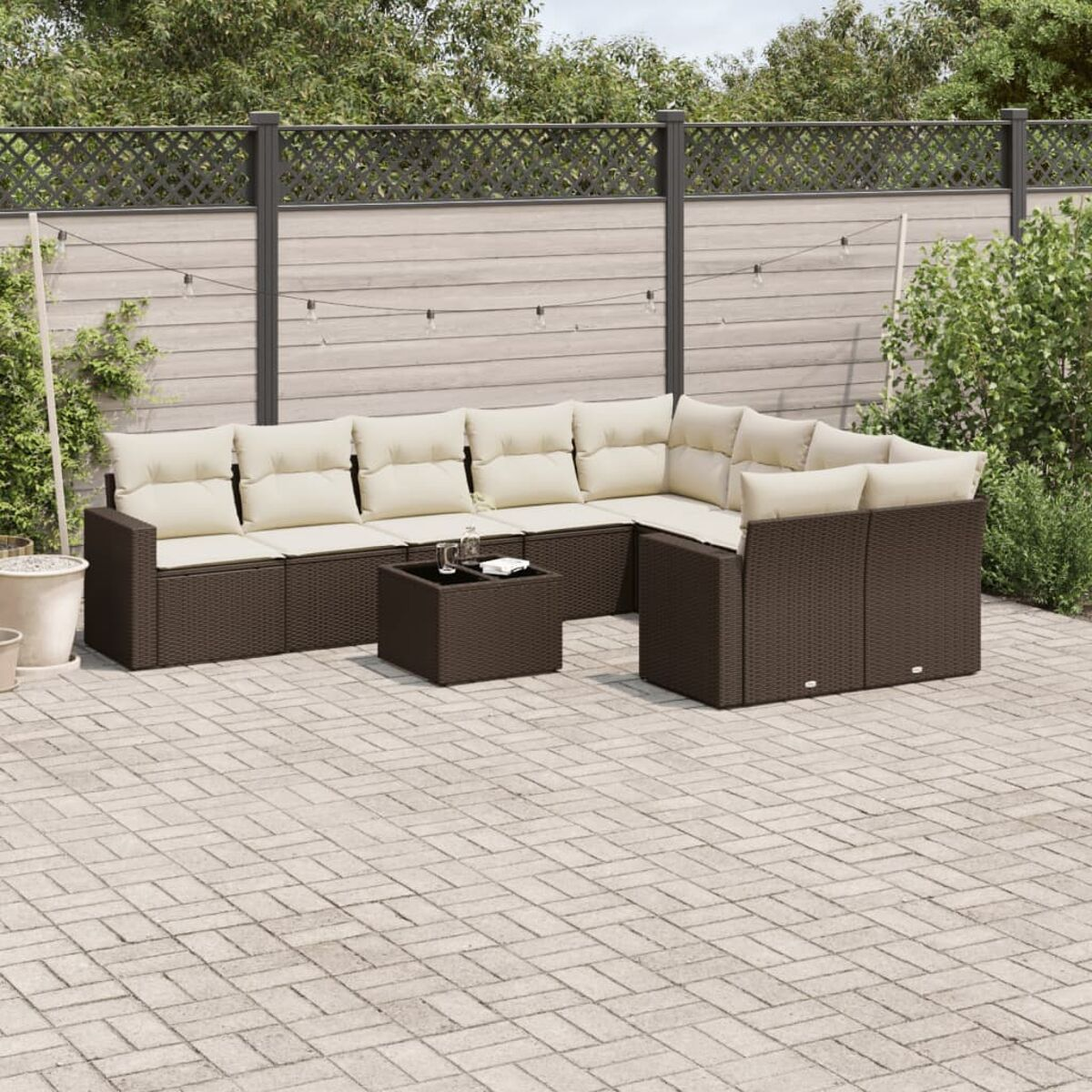 Dunkelbraunes Outdoor-Rattan-Möbelset mit beigen Kissen auf einer Ziegelterrasse mit einem Zaun.
