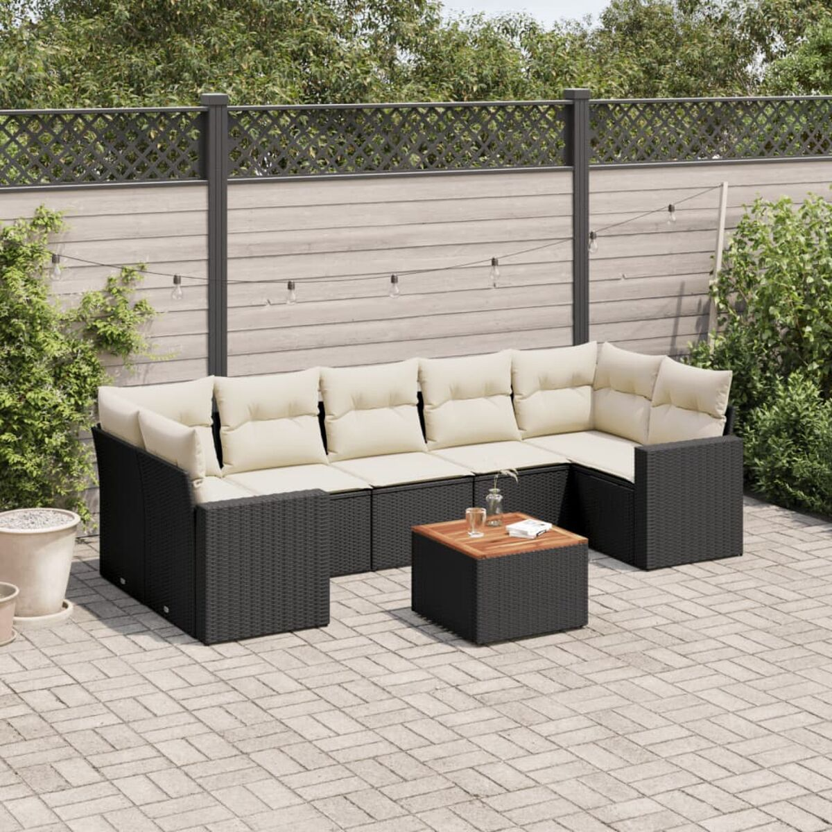 Schwarze Rattan-Outdoor-Sofagarnitur mit cremefarbenen Kissen und einem Holztisch.