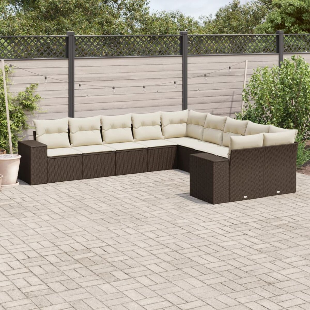 Divano componibile da esterno marrone con cuscini beige su un patio in mattoni. Recinzione e verde sullo sfondo.