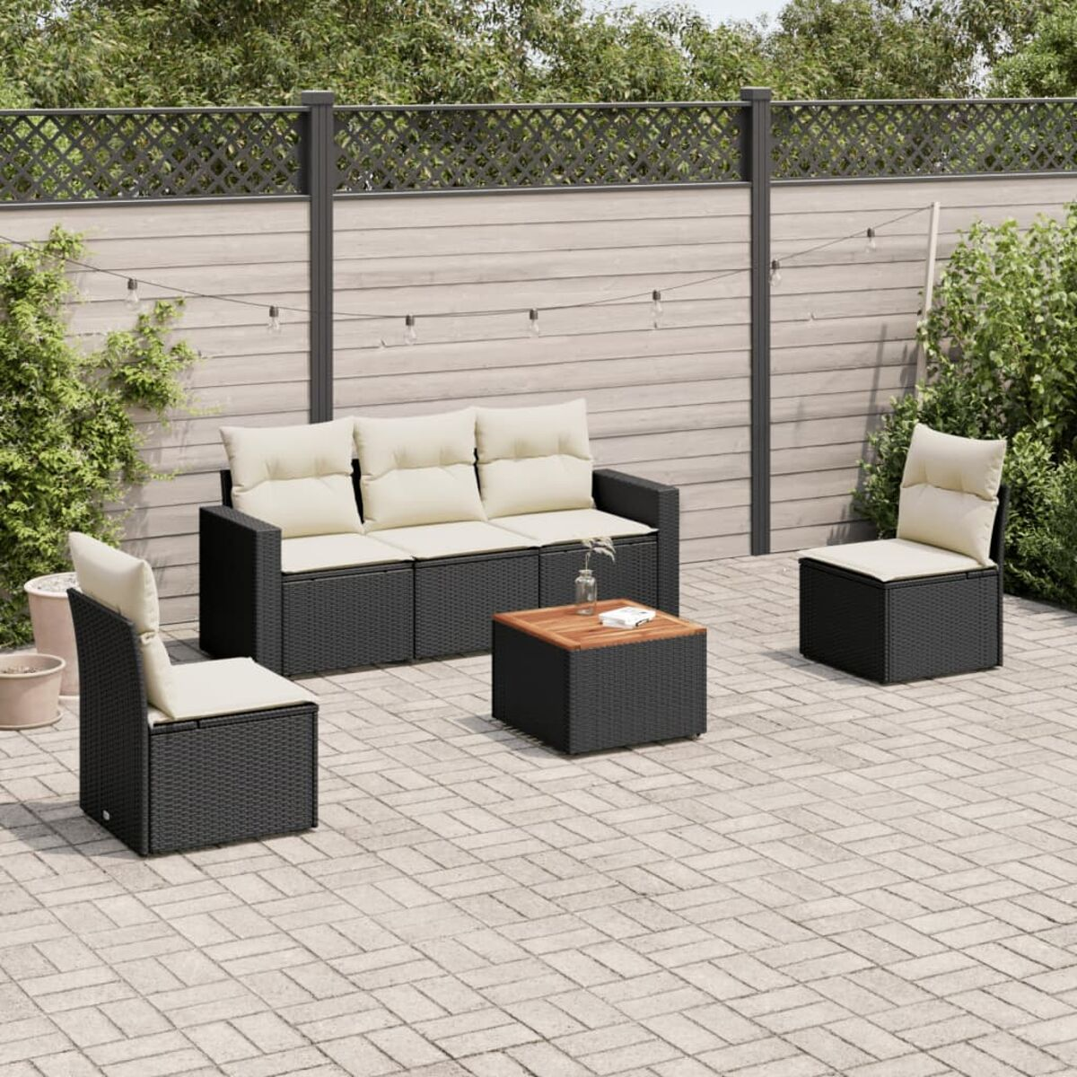 Schwarzes Rattansofa-Set mit beigen Kissen und einem Couchtisch aus Holz. Gepflasterte Terrasse.