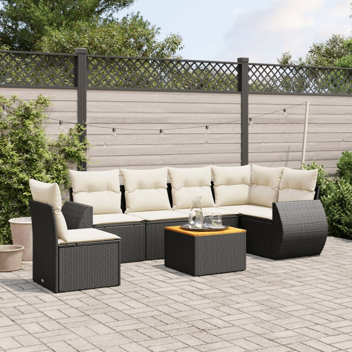 Gartenmöbel-Set aus Korbgeflecht mit Tisch und Kissen. Ziegelterrasse, Holzzaun und Pflanzen.