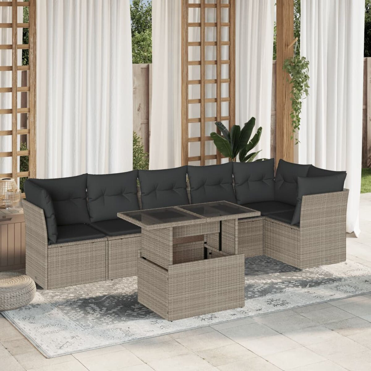 Outdoor-Wicker-Sofagarnitur mit grauen Kissen und einem hochklappbaren Couchtisch. Im Hintergrund weiße Vorhänge.