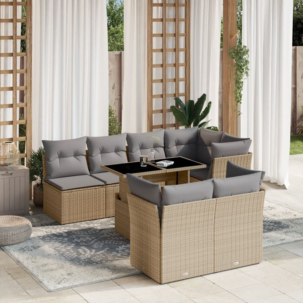 Beiges Rattan-Sofaset mit grauen Kissen, einem Tisch und einem gemusterten Teppich.