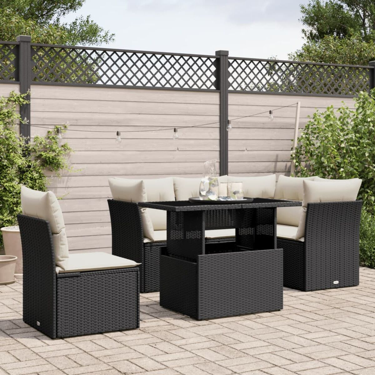 Schwarzes Outdoor-Möbelset aus Rattan mit einem Tisch. Glas und Kerzen auf dem Tisch. Grüne Pflanzen und Zaun.