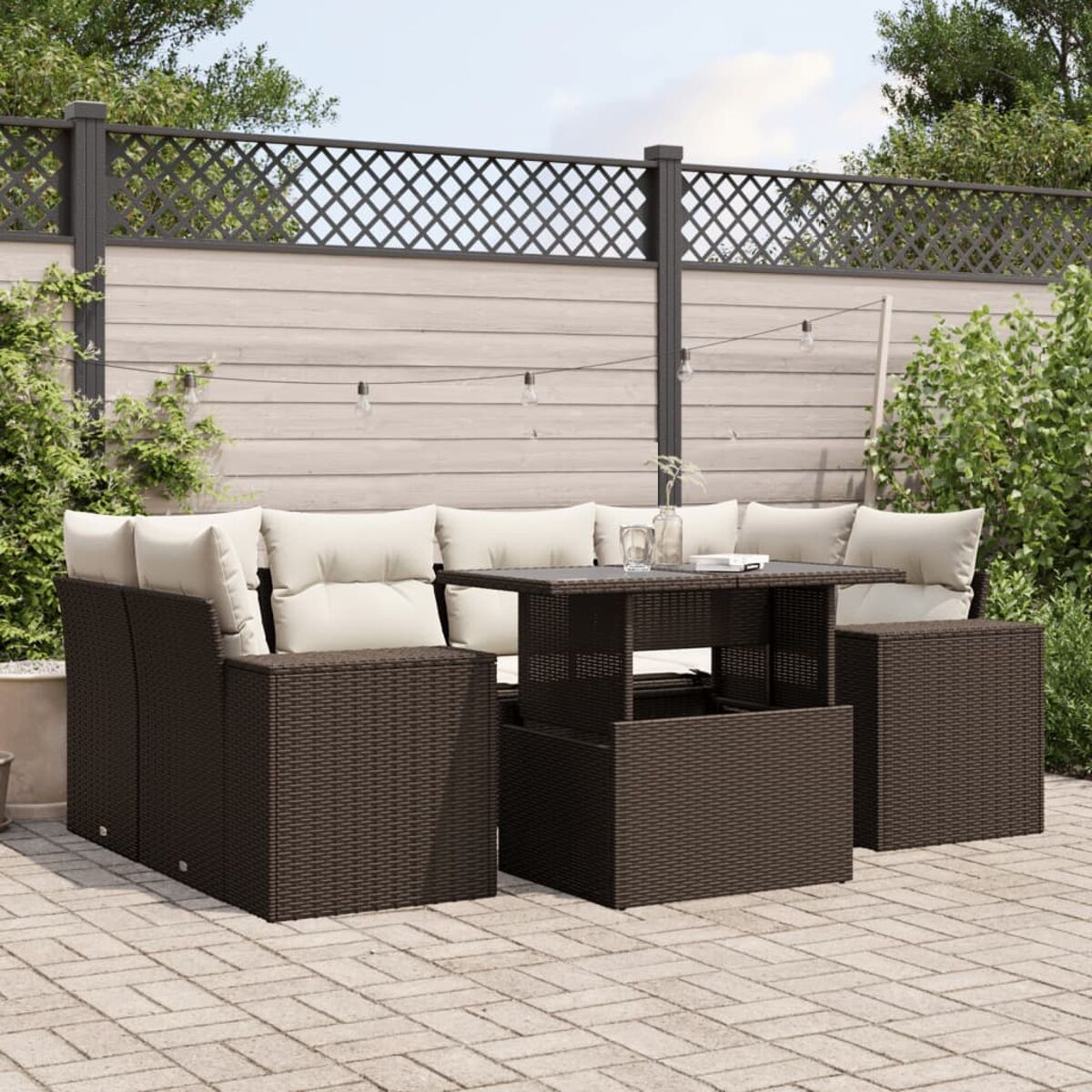 Divano angolare in rattan marrone con tavolo e cuscini color crema. Scena del patio con luci a corda.