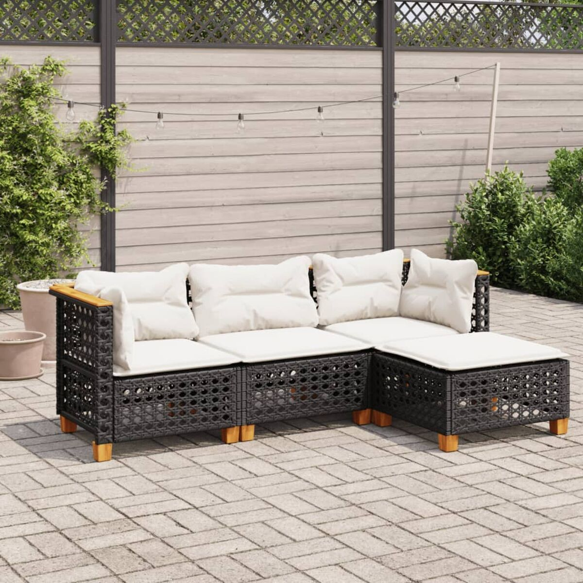 Schwarzes Rattan-Ecksofa mit cremefarbenen Kissen auf Terrasse mit Holzzaun und Pflanzen.