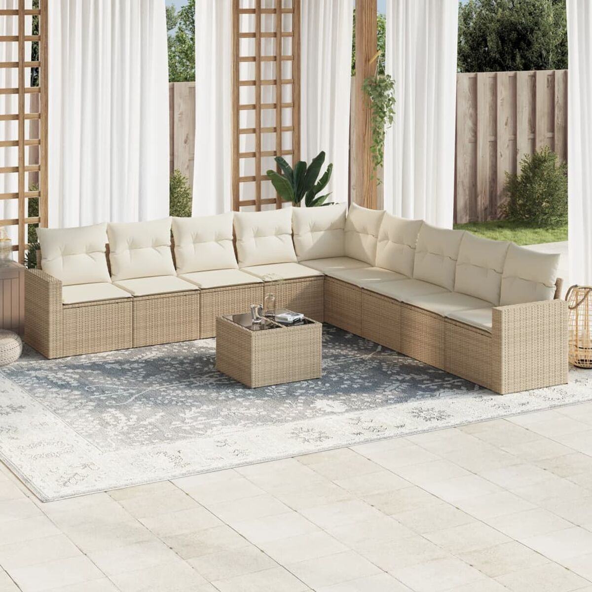 Beiges Outdoor-Ecksofa aus Rattan mit cremefarbenen Kissen, Couchtisch und Teppich. Weiße Vorhänge im Hintergrund.