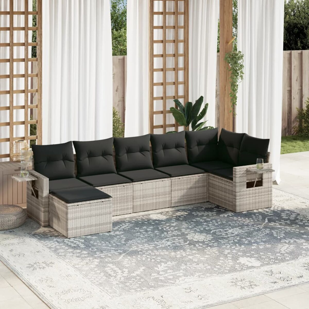 Graues Ecksofa aus Korbgeflecht mit schwarzen Kissen und Tisch, im Freien.