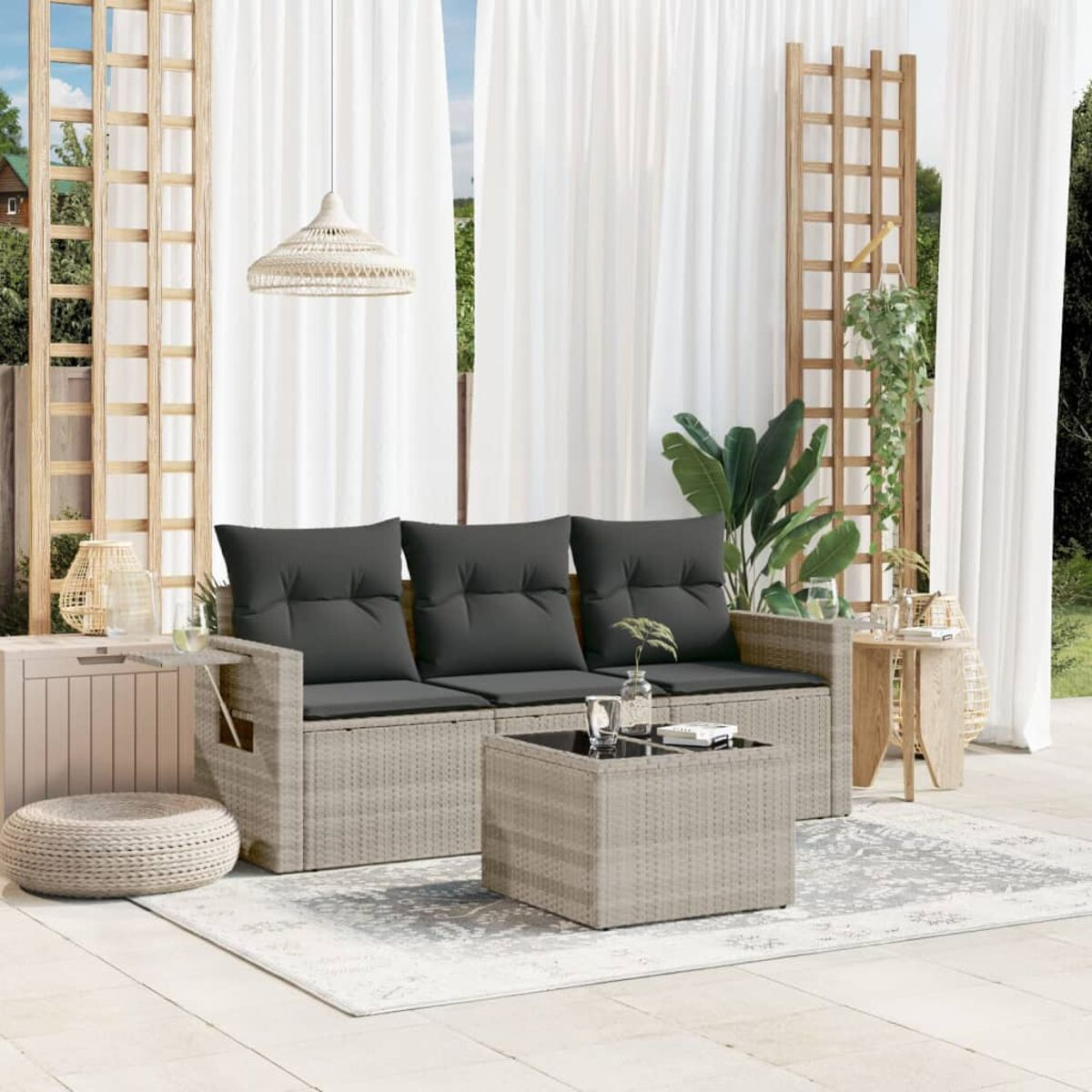 Geflochtenes Ecksofa mit grauen Kissen und Couchtisch auf einem Teppich. Vorhänge und Pflanzen sichtbar.