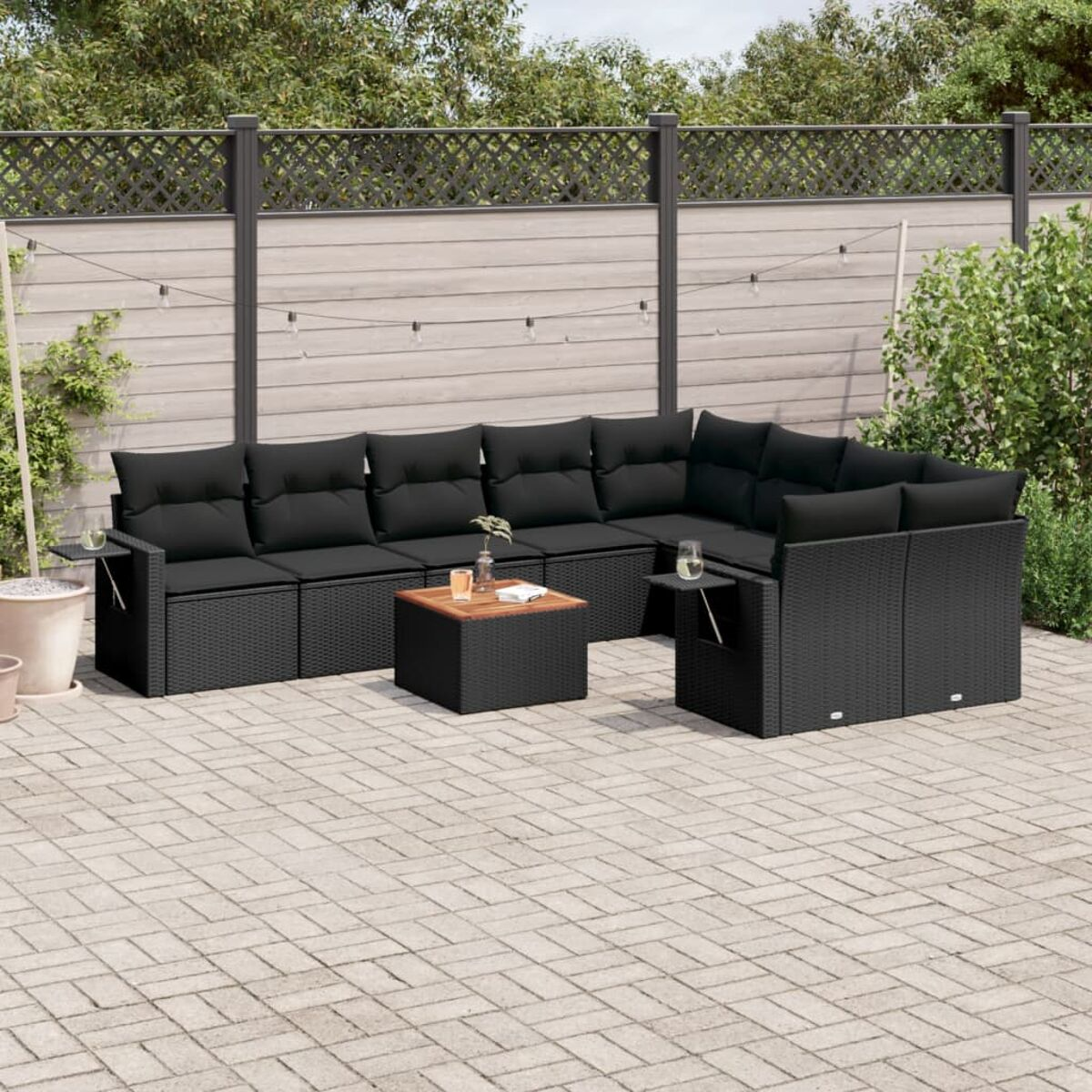 Schwarzes Rattan-Ecksofa mit schwarzen Kissen, Couchtisch und Backsteinterrasse mit Zaun.