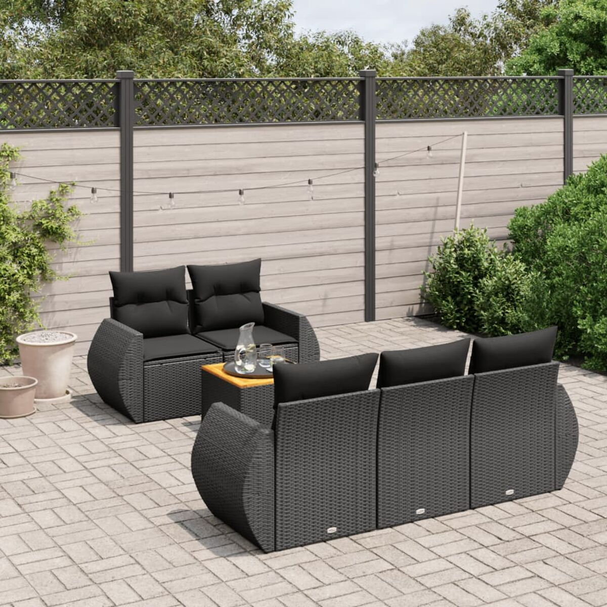 Gartenmöbel mit schwarzen Kissen, Tisch, Blick auf Holzzaun und Grün.