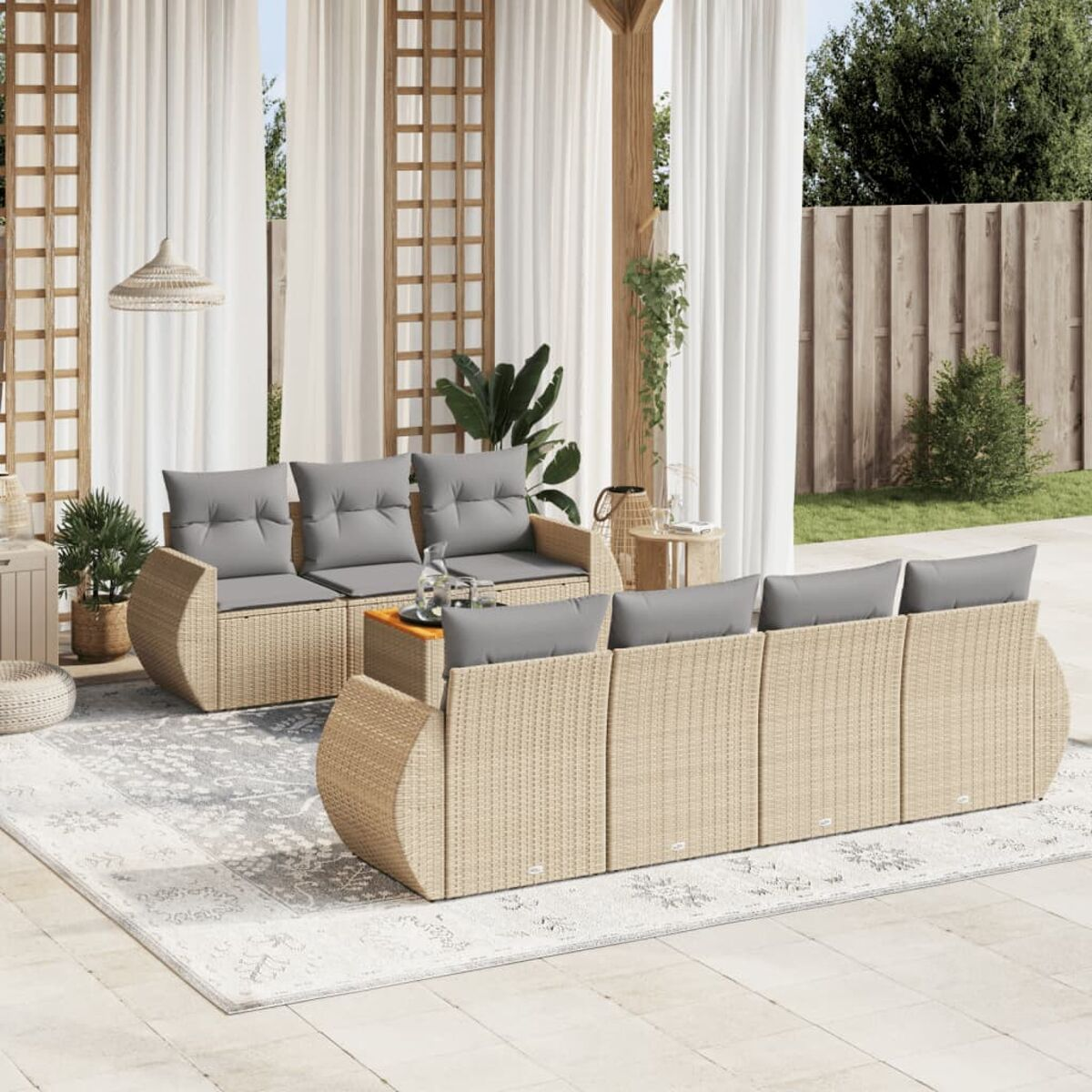 Terrassenset mit hellbraunem Rattan-Sofa, Stühlen und Couchtisch auf einem Teppich mit Vorhängen.