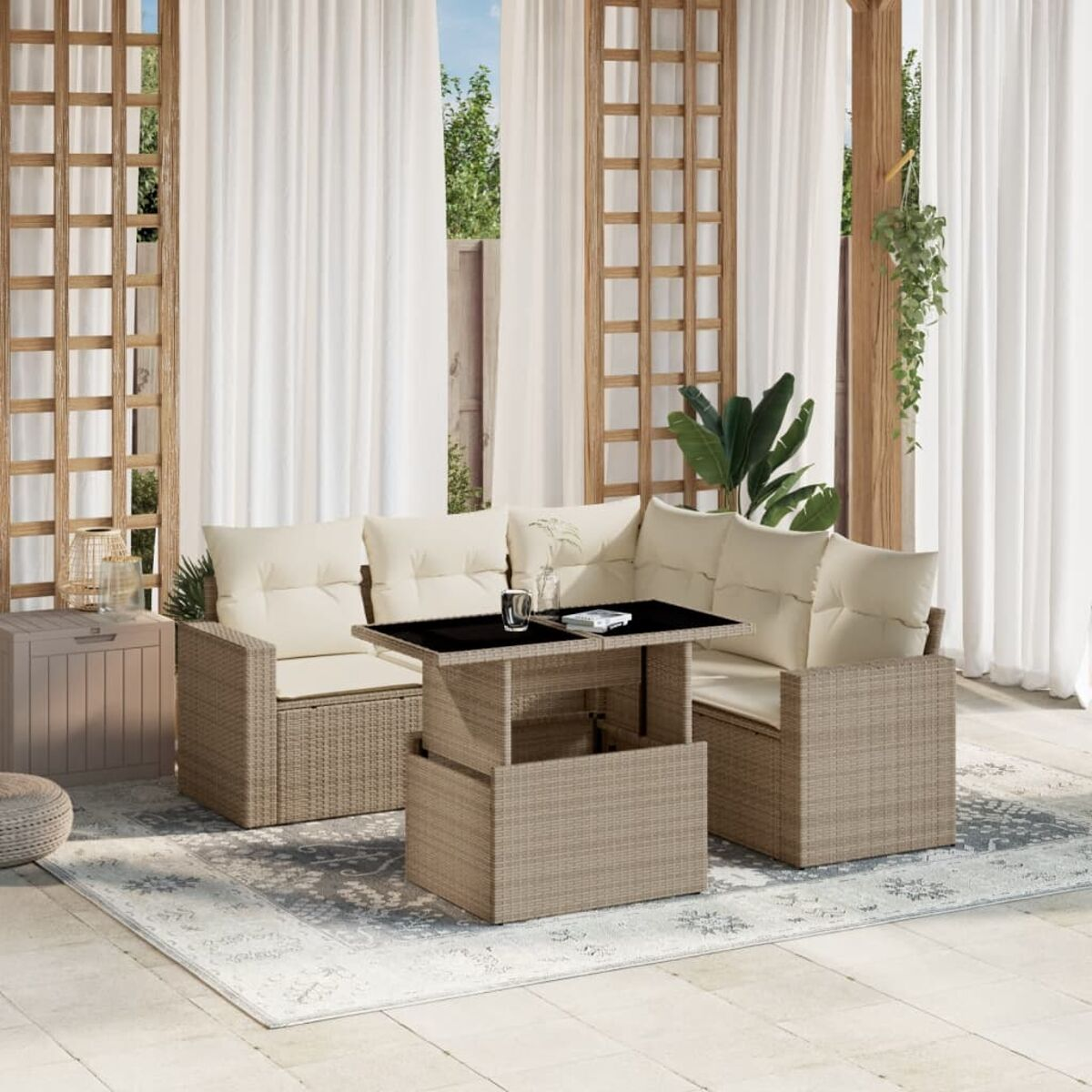 Set di sedute da esterno con tavolo con piano sollevabile su un tappeto fantasia, in un giardino. Tende sullo sfondo.