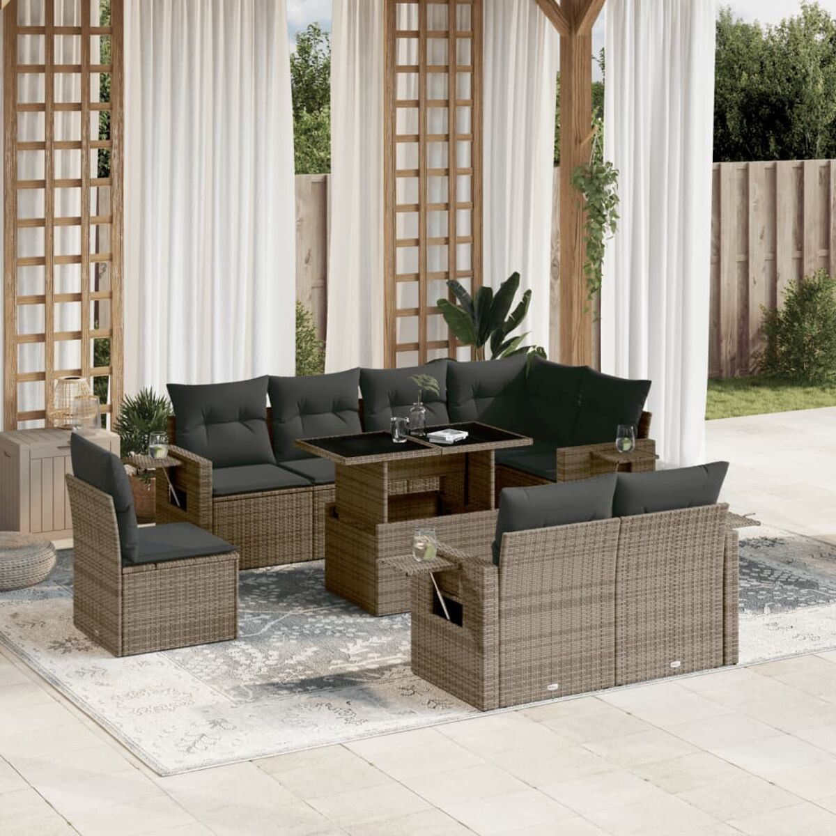 Rattansofa-Set mit dunkelgrauen Kissen auf einer Terrasse. Glastisch in der Mitte. Vorhänge im Hintergrund.