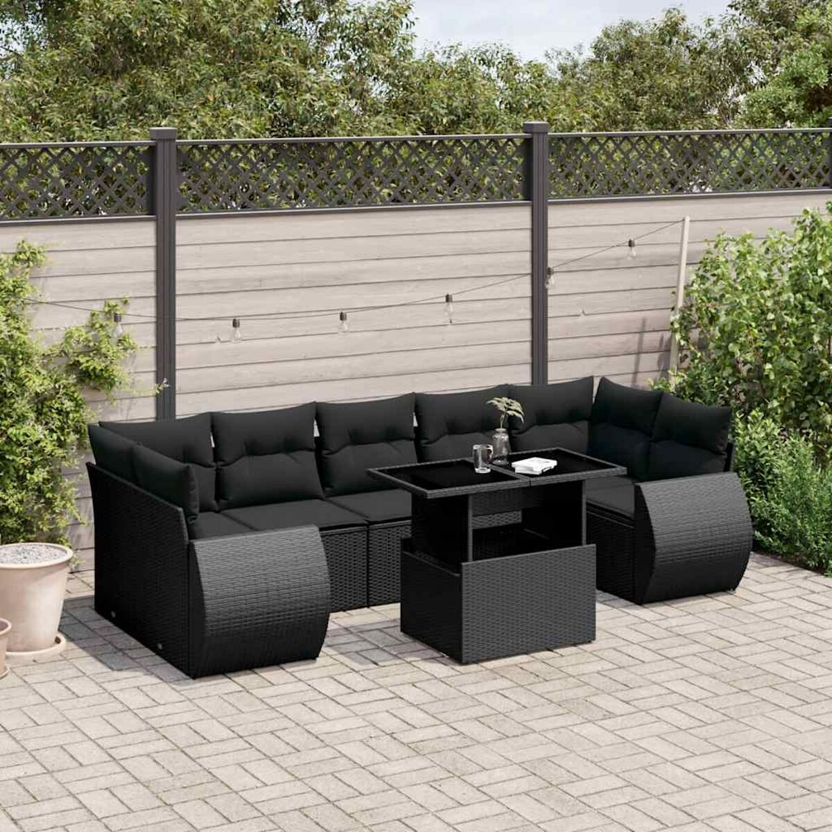 Schwarzes Korbmöbel-Ecksofa mit Tisch auf einer Backstein-Terrasse in einem Garten.