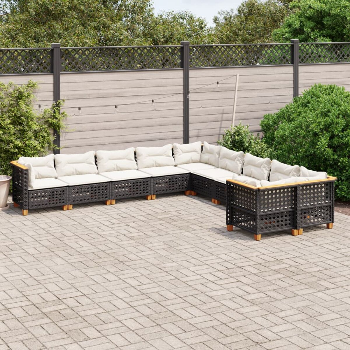Schwarzes Outdoor-Ecksofa mit cremefarbenen Kissen auf gepflasterter Terrasse, umgeben von Grün.