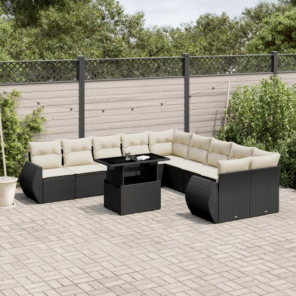 Schwarzes Rattan-Ecksofa mit cremefarbenen Kissen, Couchtisch und Backsteinterrasse mit Zaun.