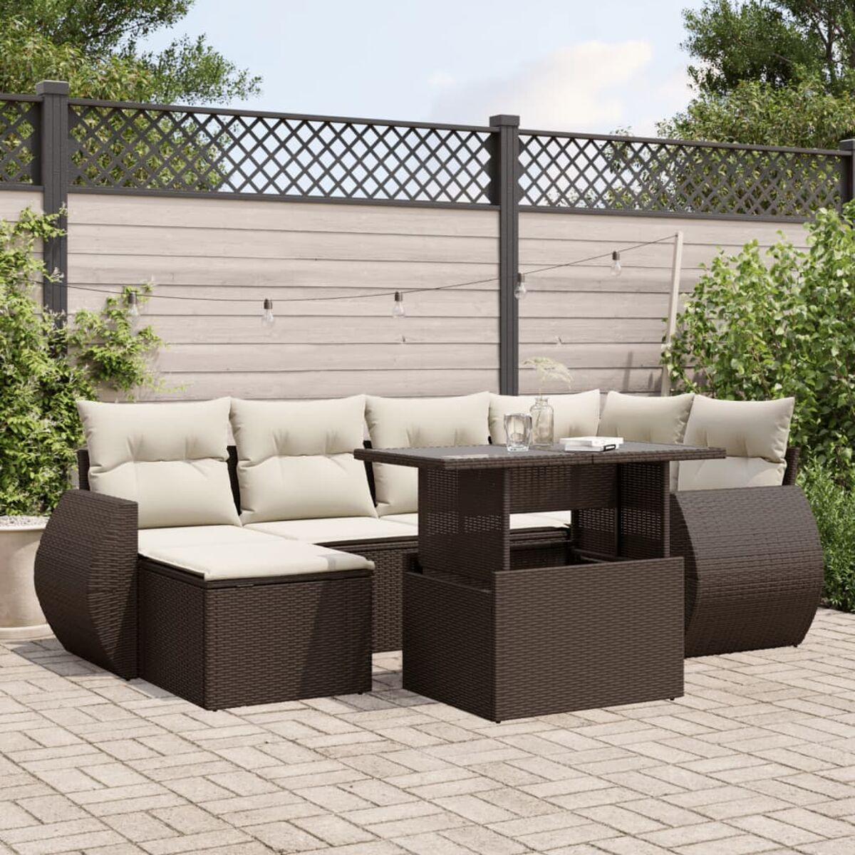 Set di mobili da esterno in vimini marrone su un patio. Include un divano, un tavolo e piante.
