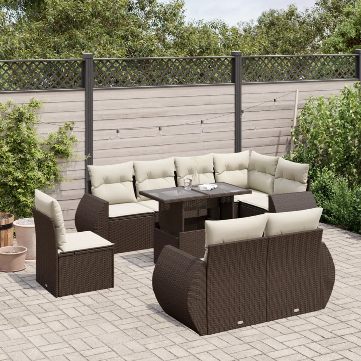 Braunes Sitzmöbel-Set aus Korbgeflecht mit grauen Kissen und einem Tisch auf einer Terrasse. Weiße Vorhänge und Holzstruktur im Hintergrund.