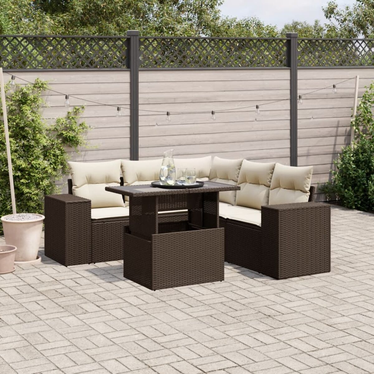 Outdoor-Ecksofa mit Tisch, beige Kissen. Ziegelterrasse, Holzzaun und Pflanzen im Hintergrund.