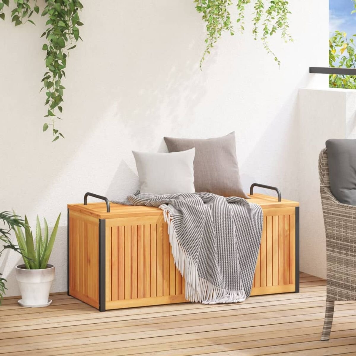 Eine hölzerne Outdoor-Aufbewahrungsbox mit Griffen und einer Decke oben drauf. Zwei Kissen sind sichtbar.