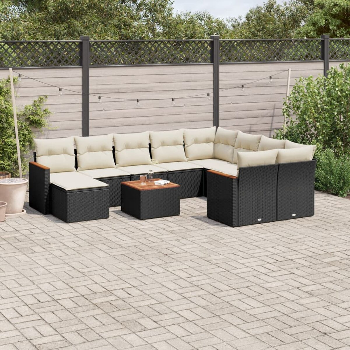 Schwarze Korbmöbel-Garten-Sitzgruppe mit beigen Kissen auf einer Terrasse mit Zaun und Pflanzen.