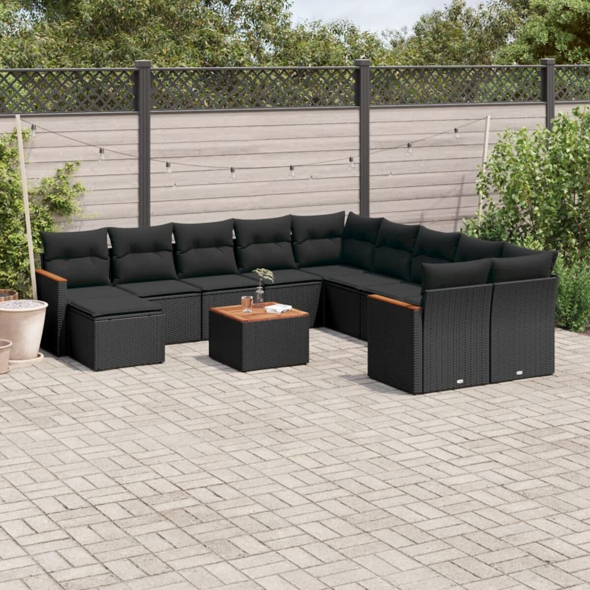 Ein schwarzes Eck-Rattan-Sofaset mit schwarzen Kissen, einem Holztisch und Garten.
