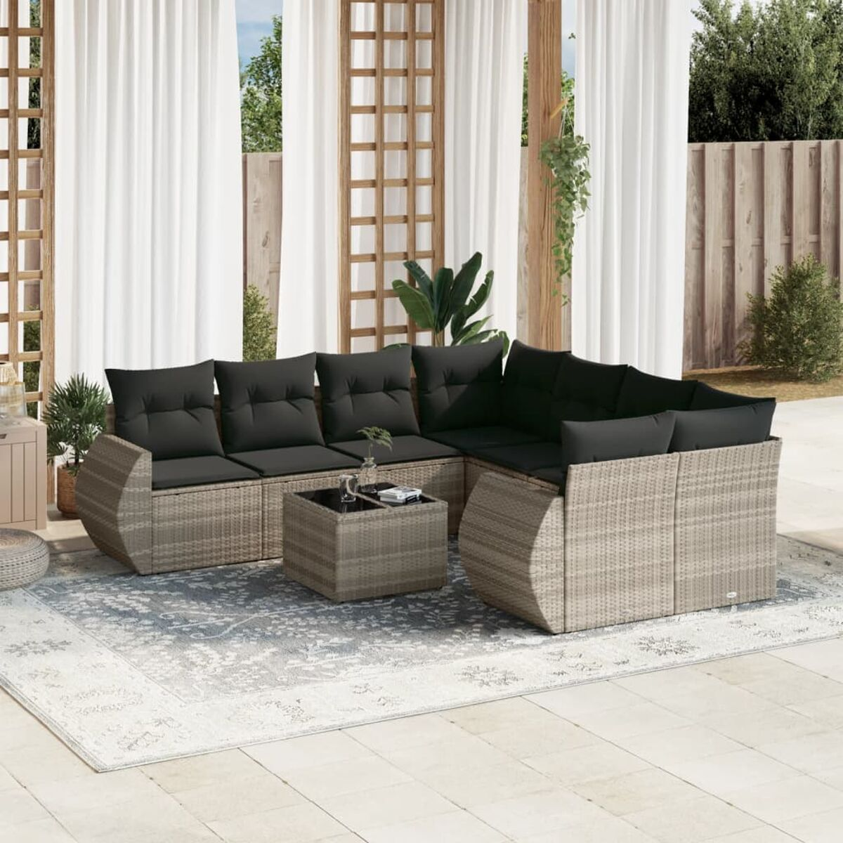 Geflochtenes Outdoor-Ecksofa mit schwarzen Kissen und einem quadratischen Couchtisch. Beiger Teppich und weiße Vorhänge im Hintergrund.