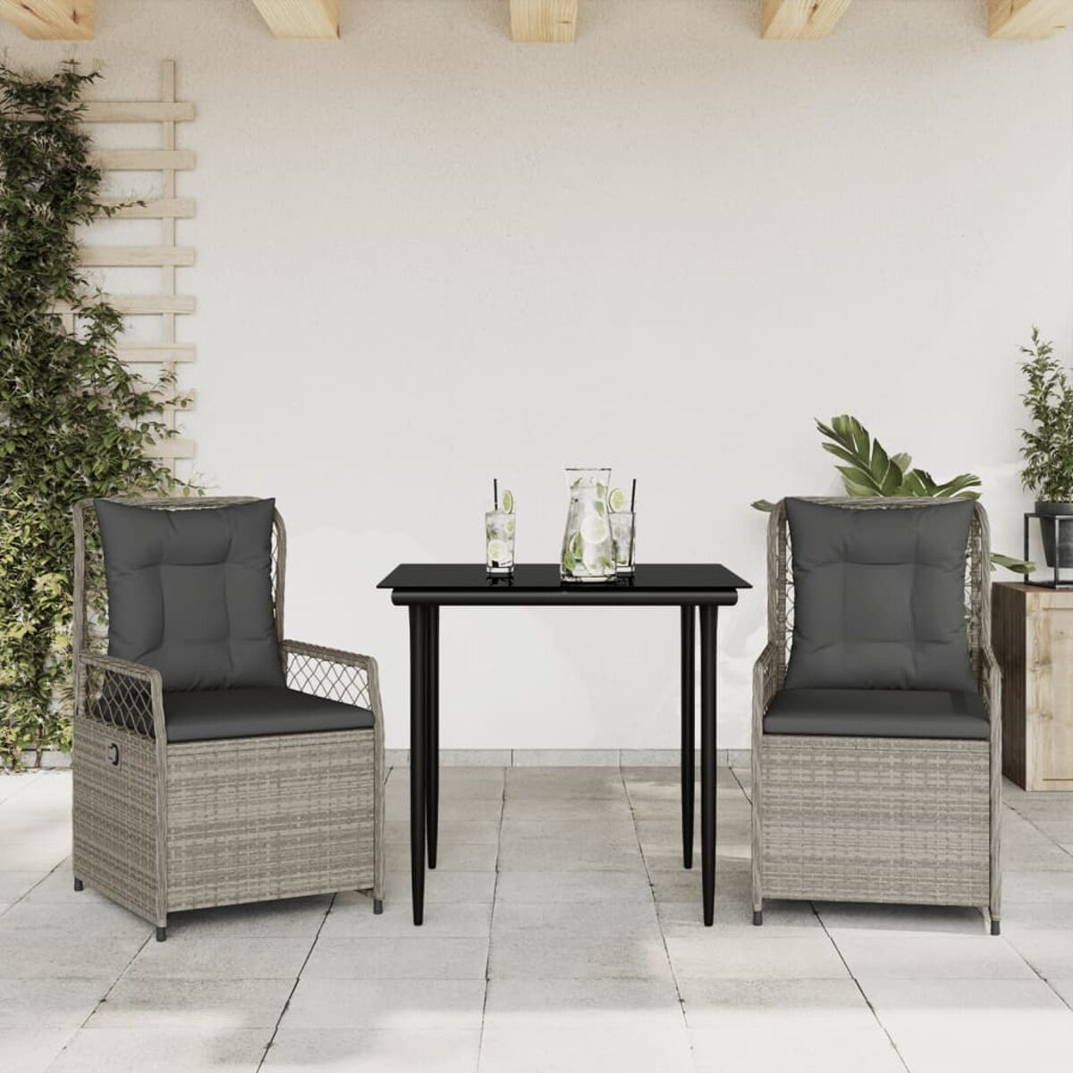 Zwei graue Korbstühle mit schwarzem Tisch, Getränken und Pflanzen auf der Terrasse, weißer Wandhintergrund.