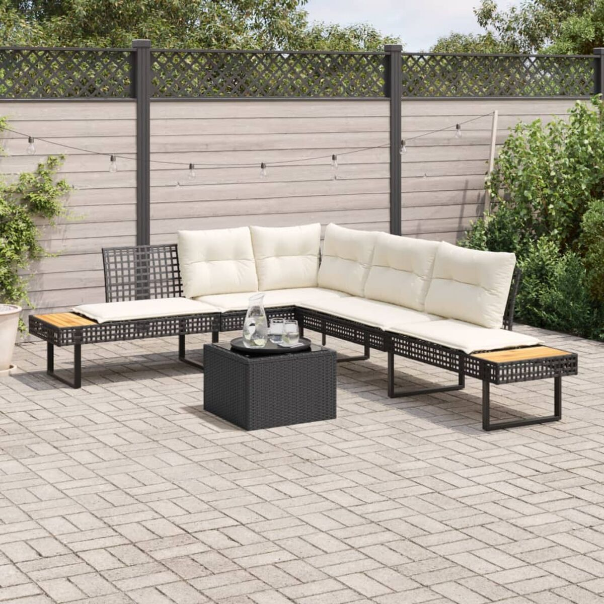 Divano angolare in vimini nero con cuscini color crema e tavolo nero su patio.