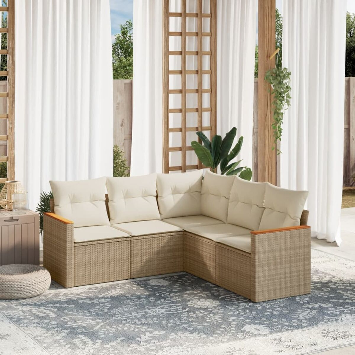 Beiges L-förmiges Rattan-Sofa mit cremefarbenen Kissen, auf einem gemusterten Teppich, im Freien mit Holzakzenten.