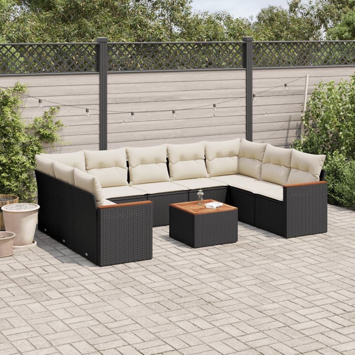 Schwarzes Korbmöbel-Ecksofa mit beigen Kissen und Holztisch auf der Terrasse.