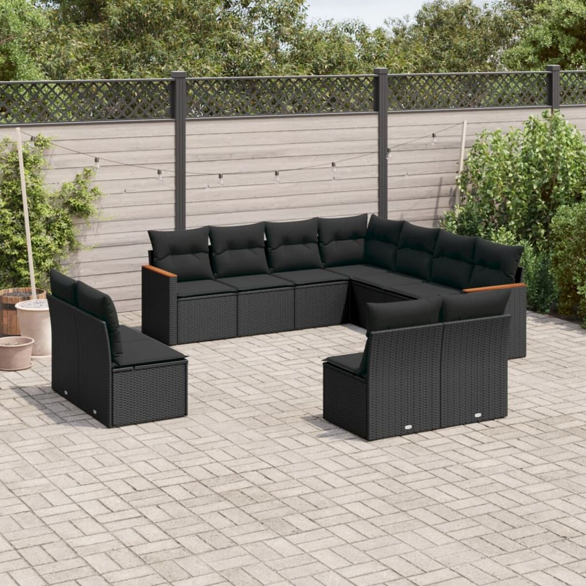 Schwarzes Outdoor-Ecksofa aus Korbgeflecht mit Kissen. Zwei Stühle und ein Couchtisch im Garten.
